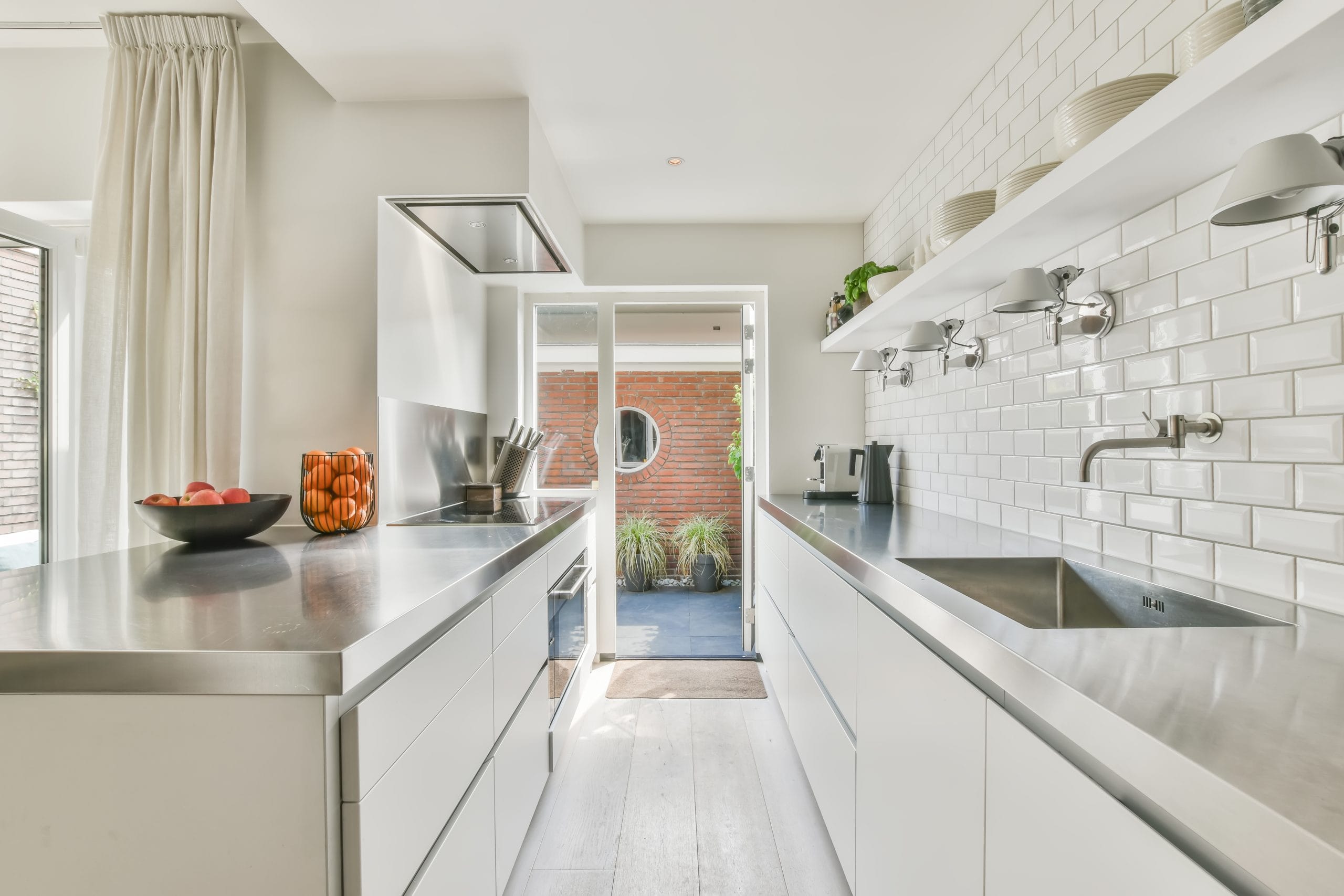 Bright modern kitchen with white cabinets, stainless steel countertops, and a door leading to a patio.